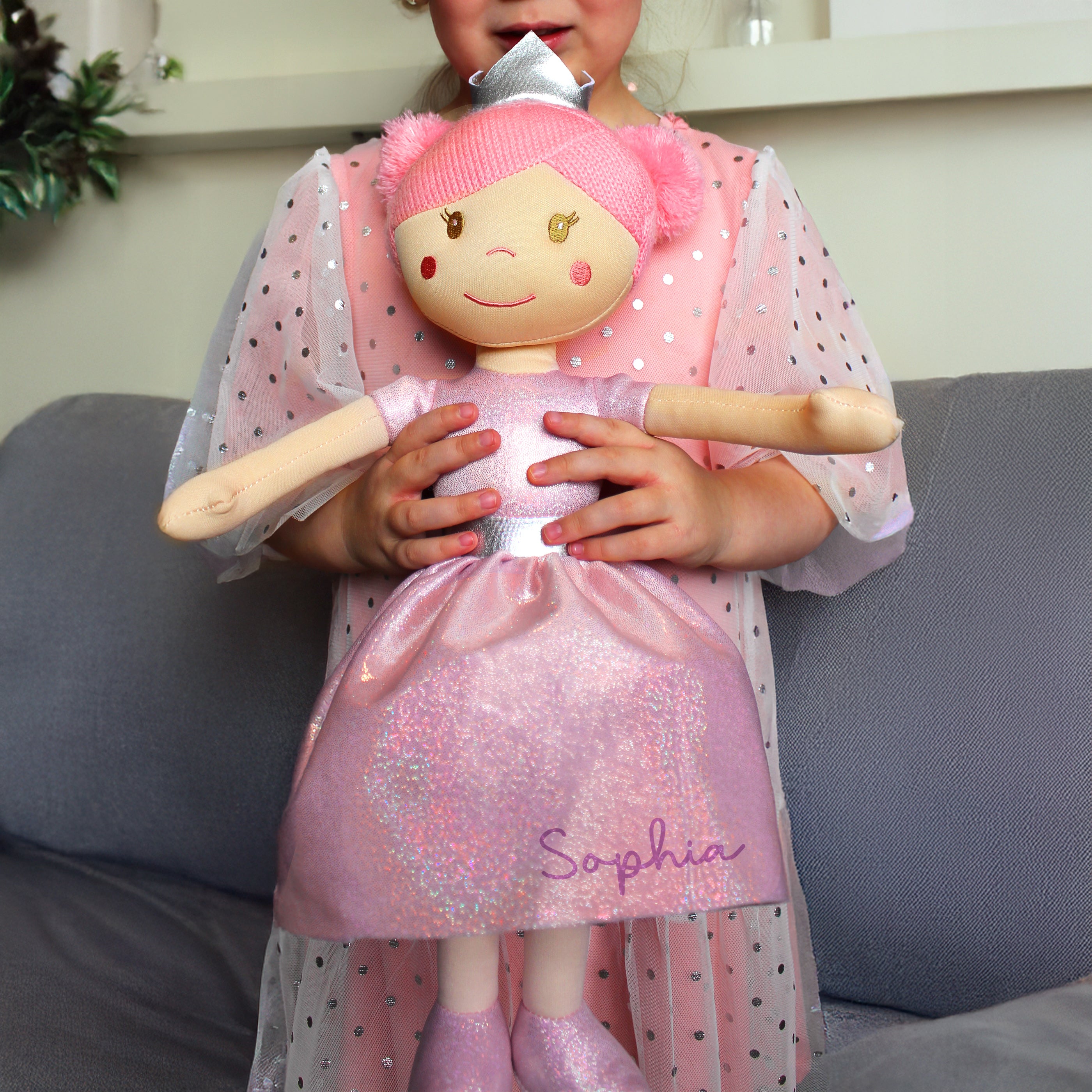 Child holding a doll named 'Sophia' in a pink outfit with a polka dot cape.