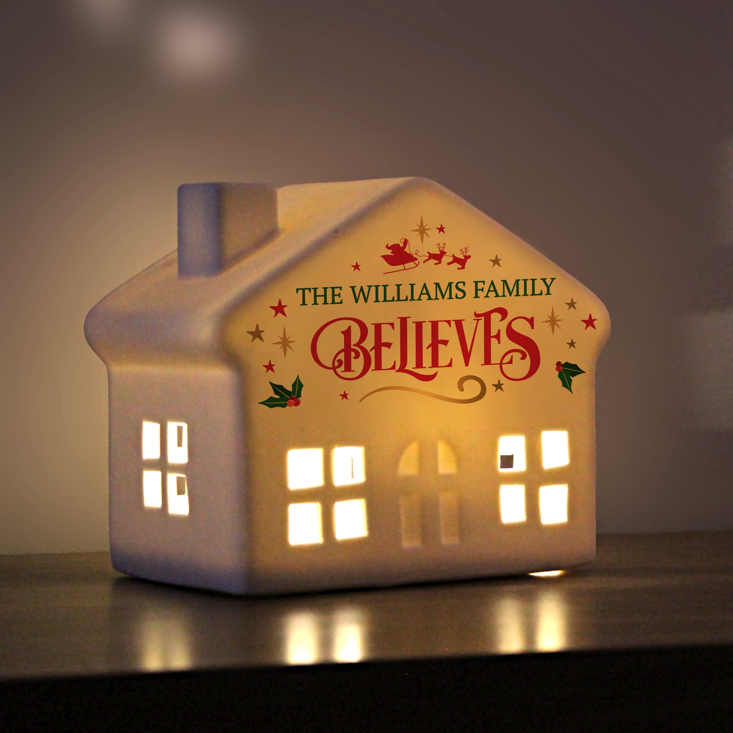 Small personalised ceramic light-up house displayed on a mantelpiece or shelf.