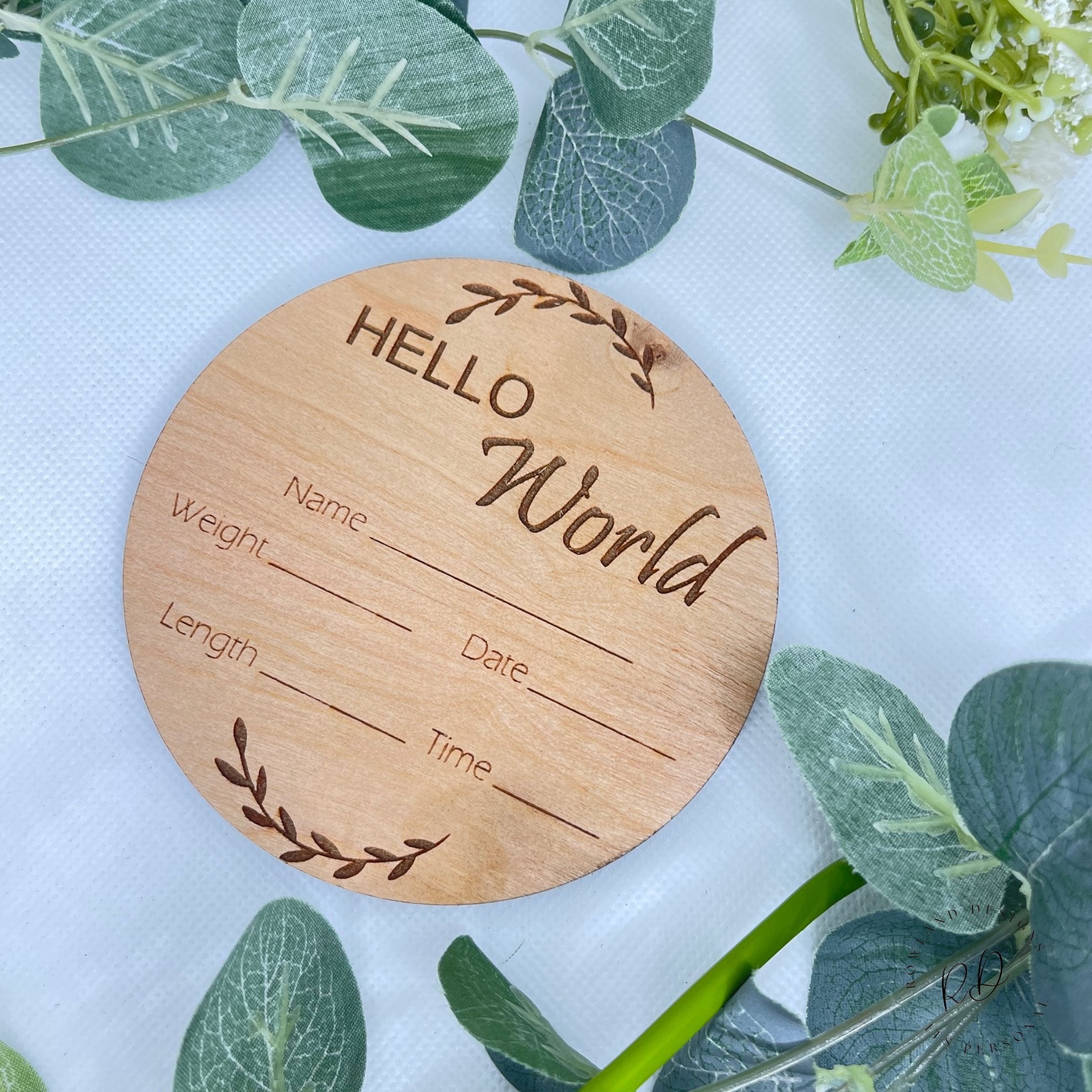 Close-up of the "Hello World" plaque with handwritten baby details and a leaf design.