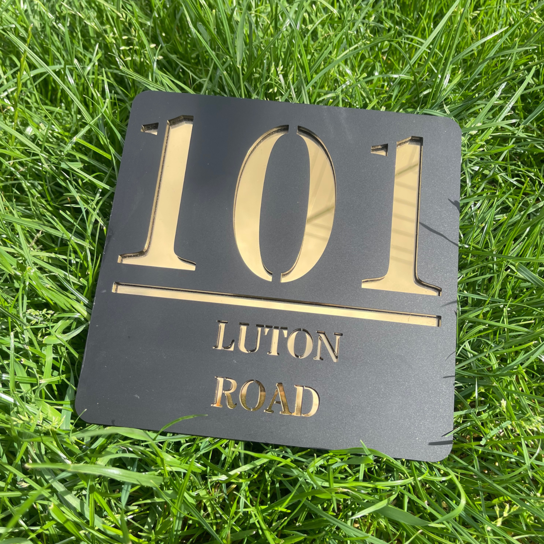A full, front-on view of the contemporary square house sign in matte black with gold backing, showing the custom house number and street name.