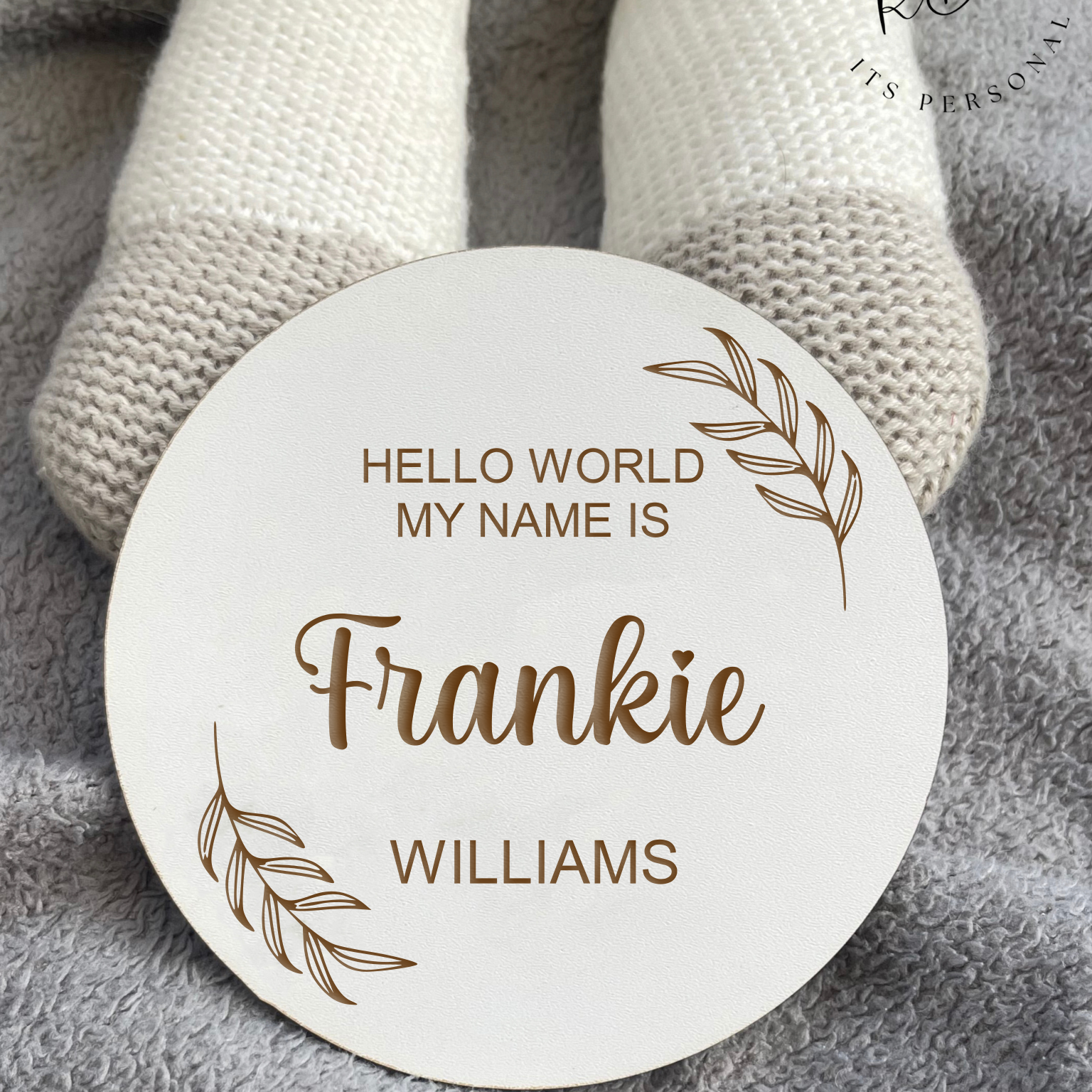 Modern white nursery reveal plaque with leaf motif for gender-neutral baby announcements.