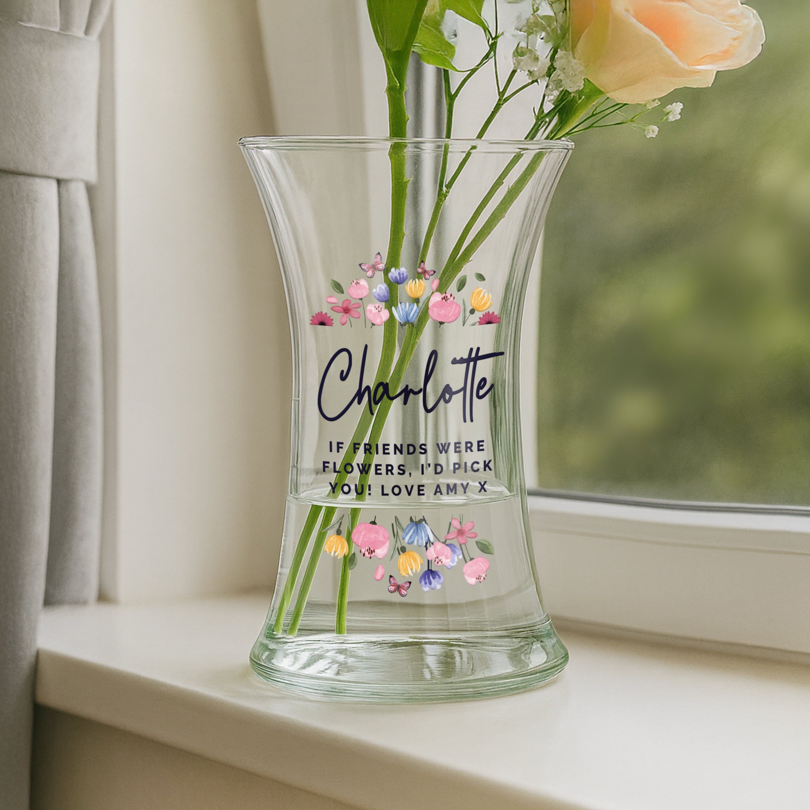 Clear glass vase with floral design and text on a windowsill