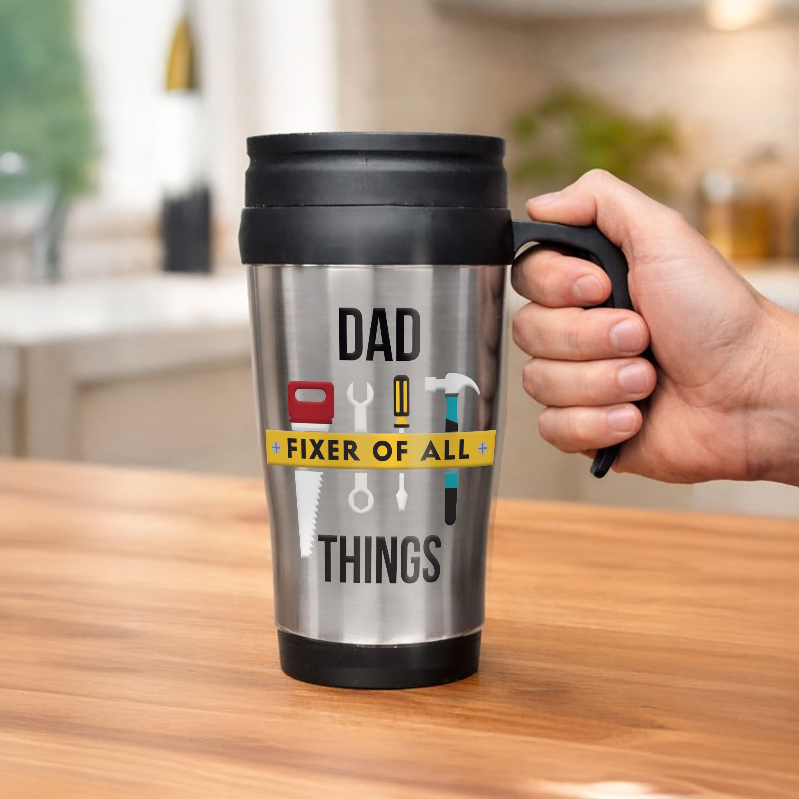 Hand holding a travel mug with 'Dad Fixer of All Things' text on a wooden surface.