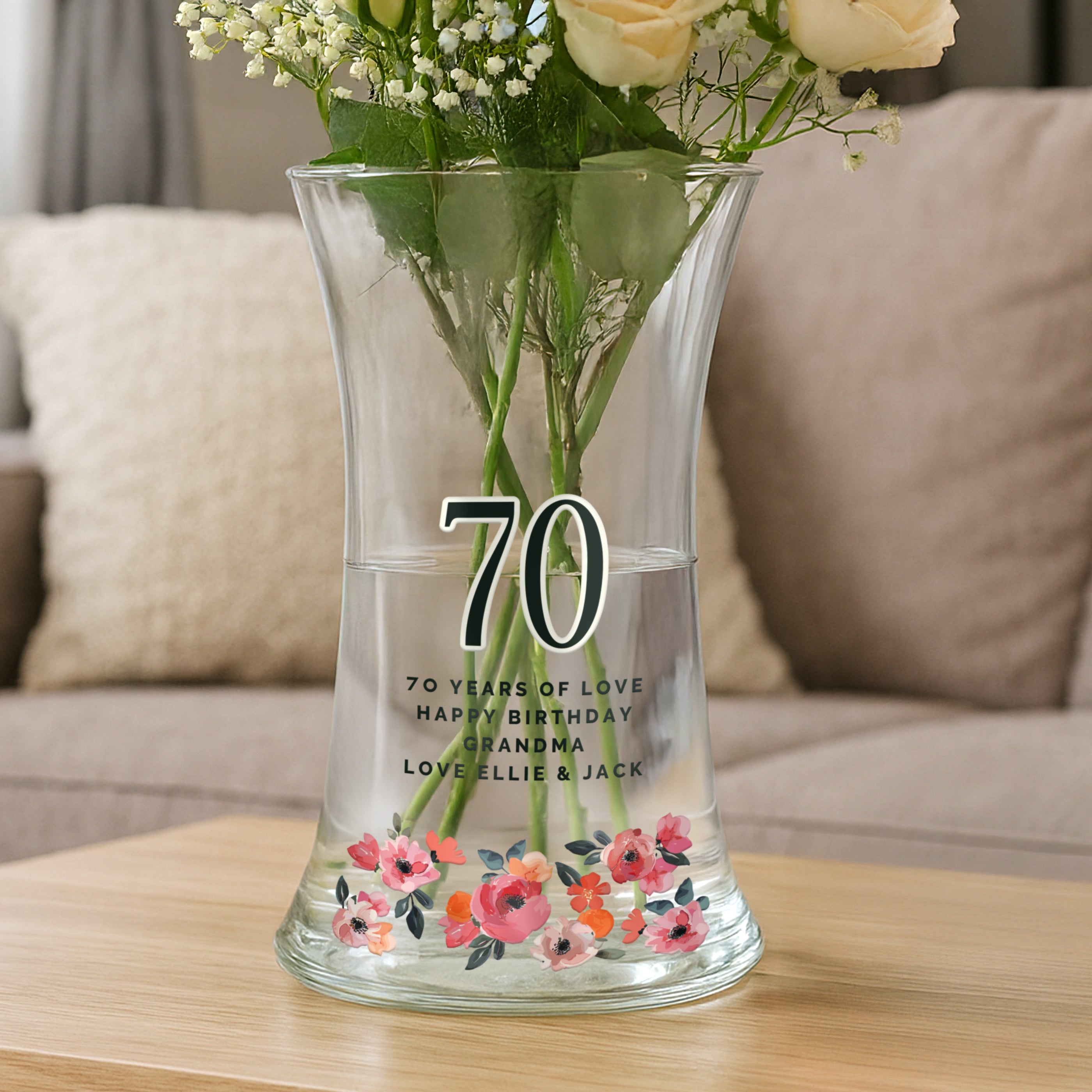 Clear glass vase with flowers and personalized text on a wooden table.