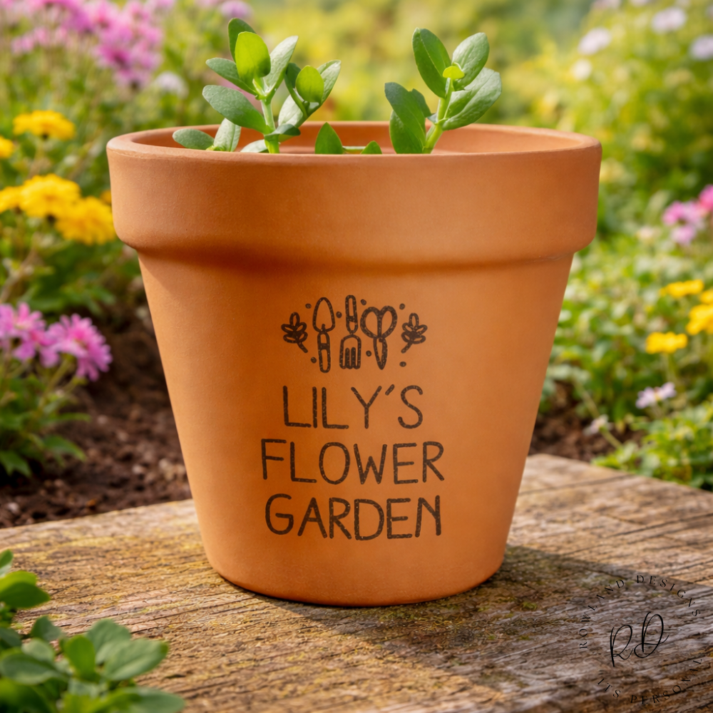 Terracotta pot with 'Lily's Flower Garden' text on a wooden surface with a garden background.