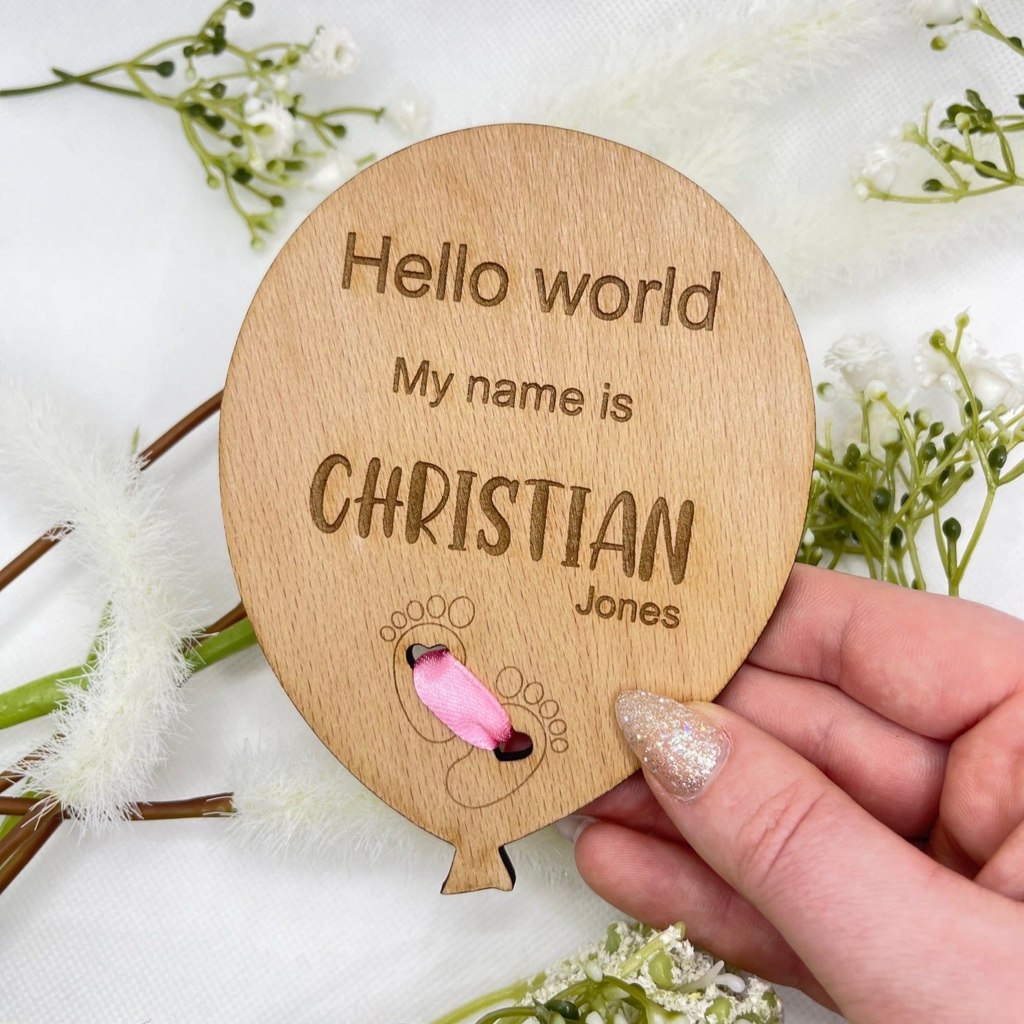 Close-up shot of the engraved feet design and the pink ribbon on a personalised baby announcement plaque.