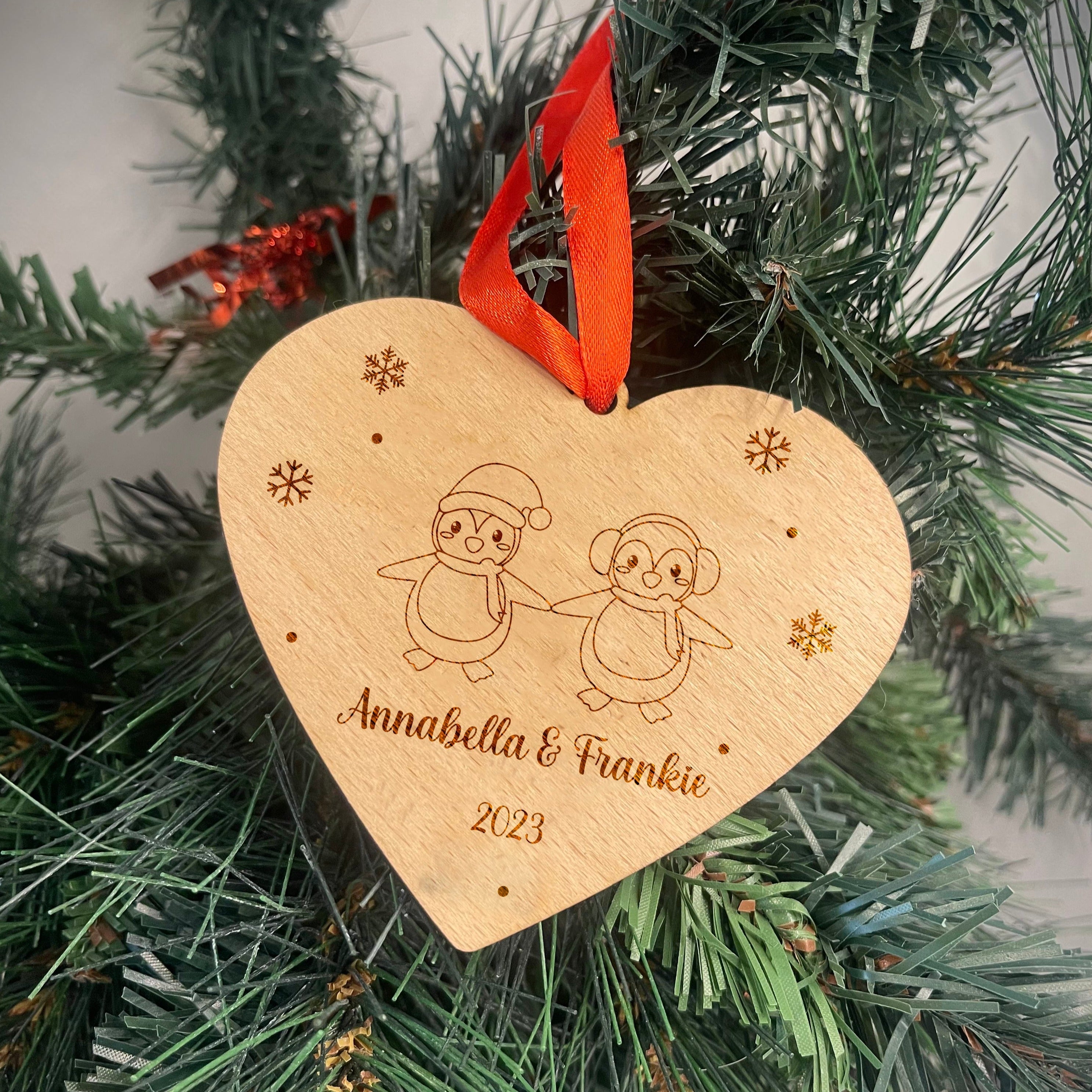 A wooden couples Christmas bauble featuring two interlocking penguins.