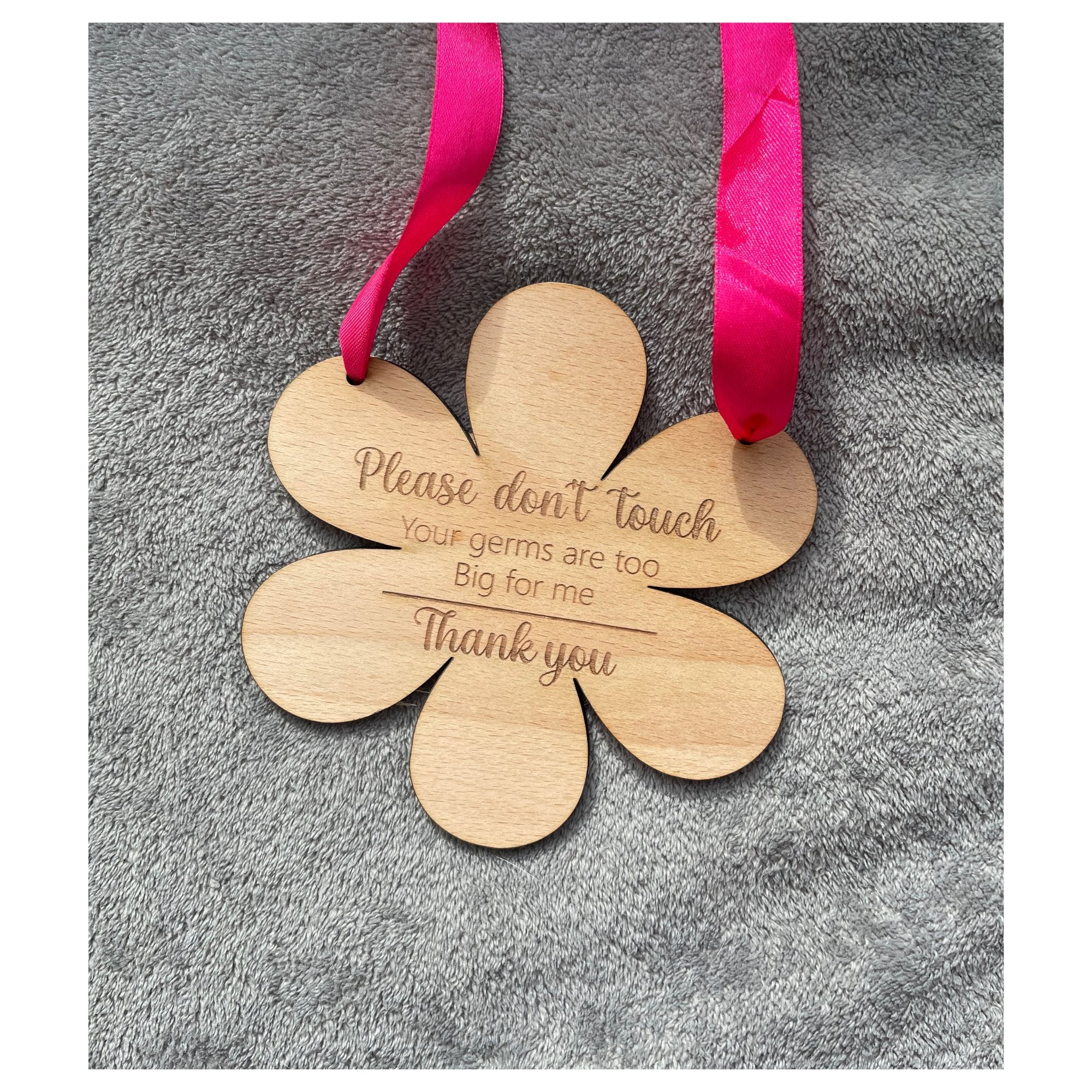 Celebrate the journey of motherhood with our protective flower-shaped beech wood hanging sign. Crafted from sturdy 4mm wood and measuring 145mm by 148mm, this enchanting piece transcends mere decor. Engraved with 'Please do not touch, your germs are too big for me, thank you,' and available with a touch of personalization through your choice of blue or pink ribbon.