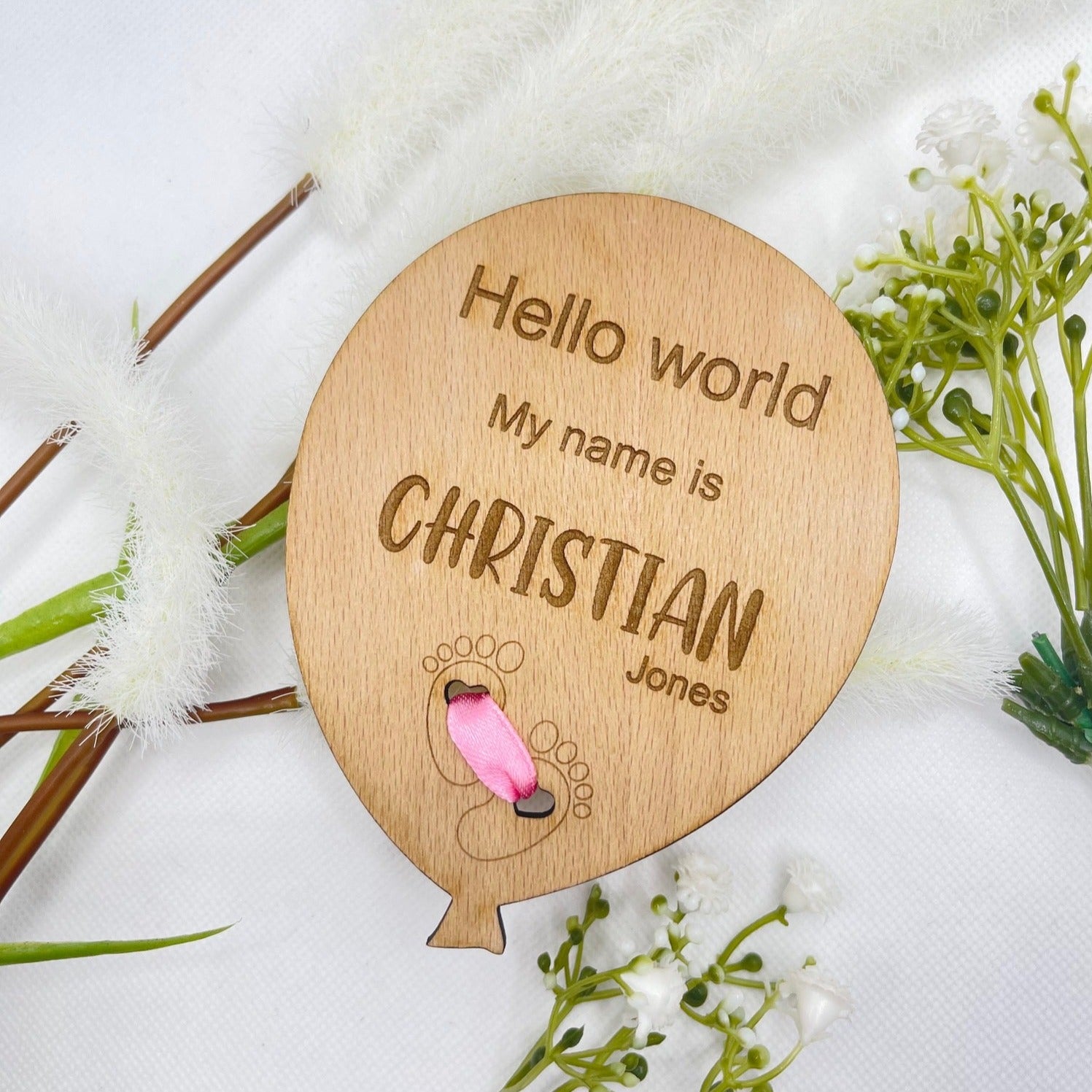 Full view of a personalised wooden baby announcement plaque featuring an adorable feet design and a pink ribbon.