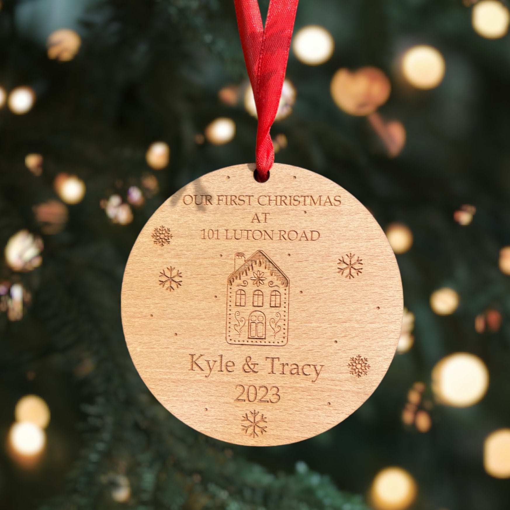 A personalised wooden round Christmas ornament with a red ribbon, featuring engraved text and designs, hanging from a Christmas tree.