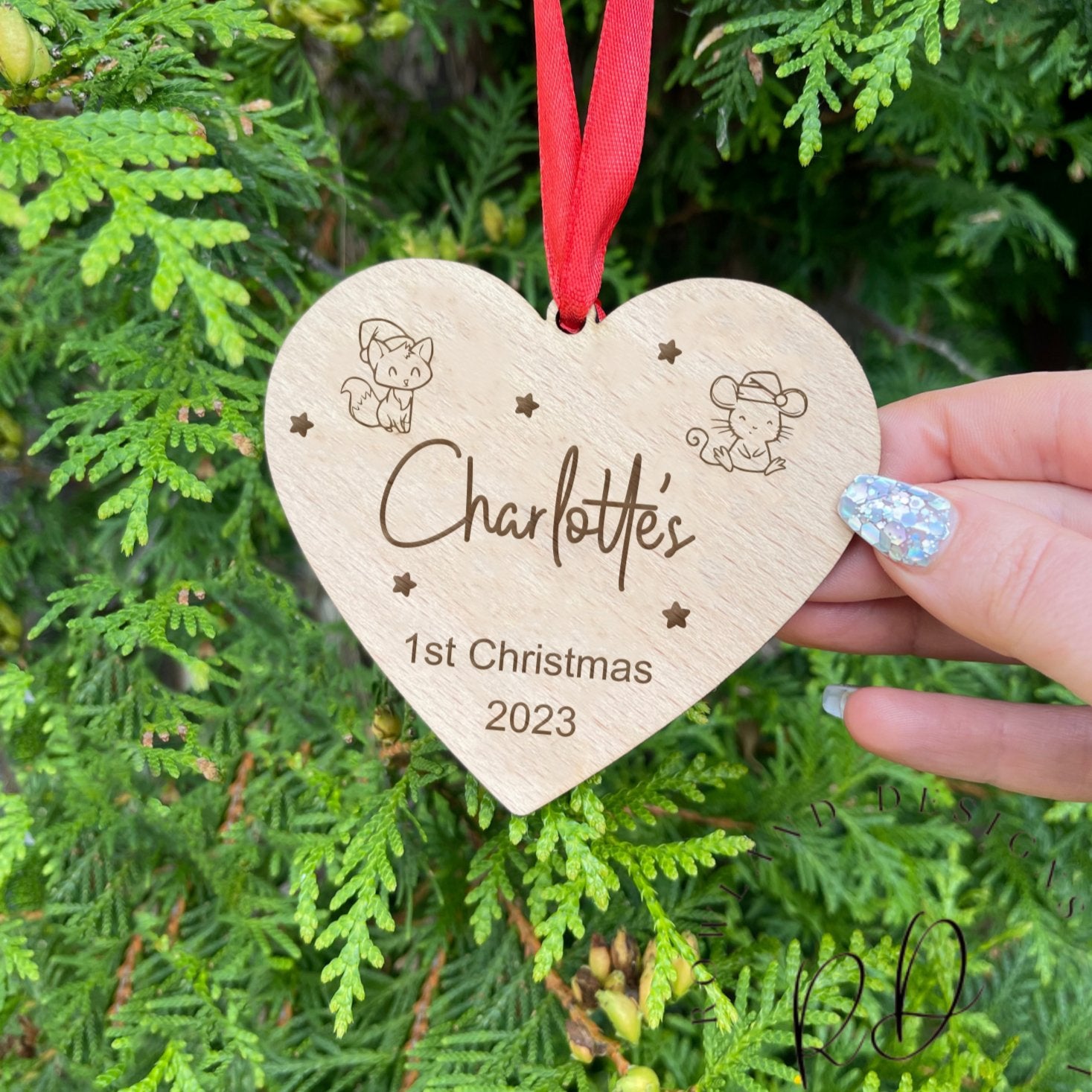 A personalised heart-shaped wooden bauble for a baby's first Christmas, with a custom name and a red ribbon.