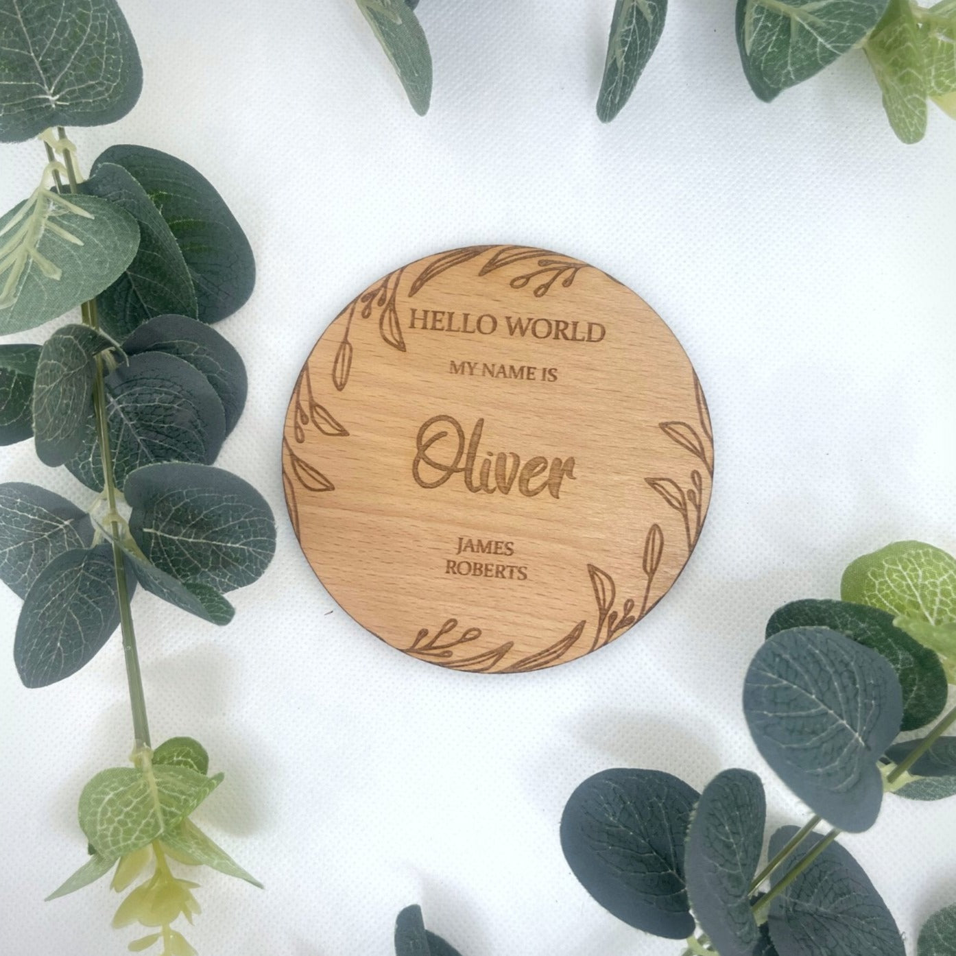Detailed close-up of the engraved baby's name and natural leaf design on a wooden announcement plaque.
