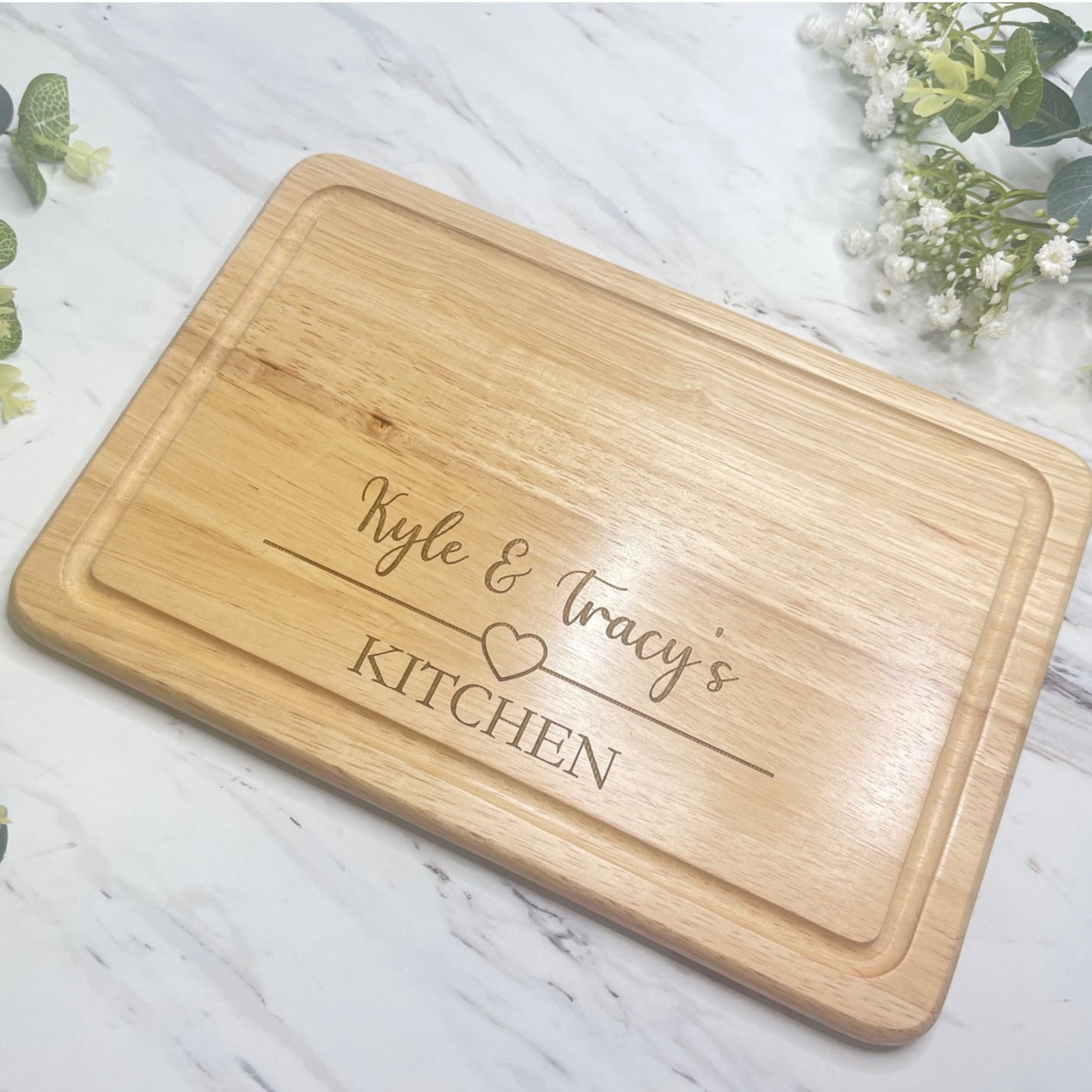 A personalised wooden chopping board with a heart design and custom engraved names.