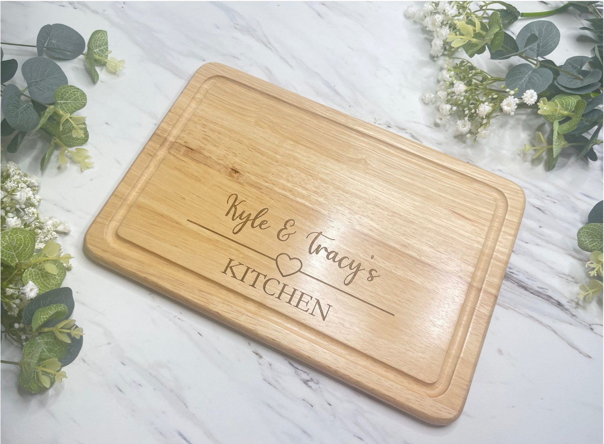 A personalised wooden chopping board with a heart design and custom engraved names.