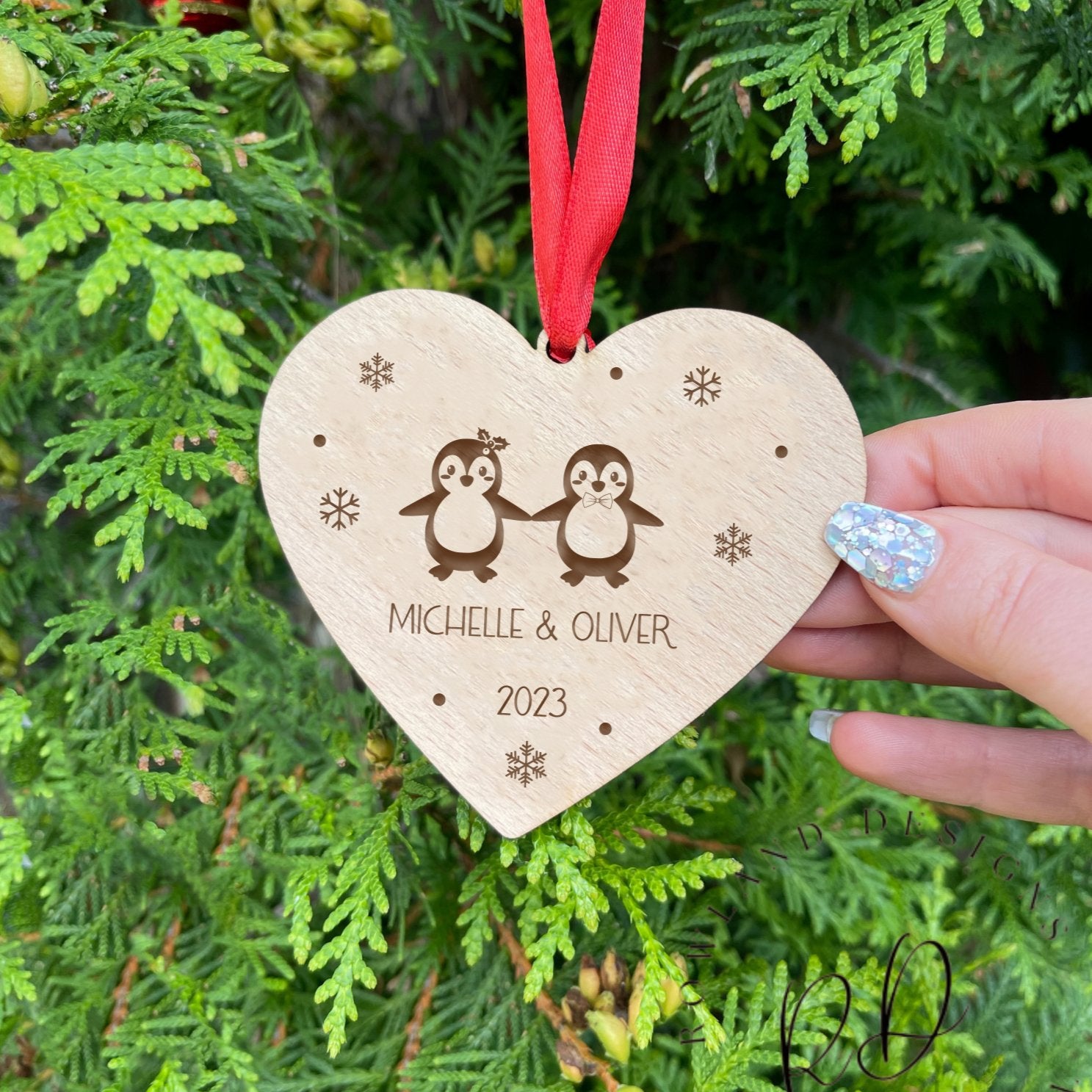 Engraved beech wood Christmas decoration showing a penguin couple, snowflakes.