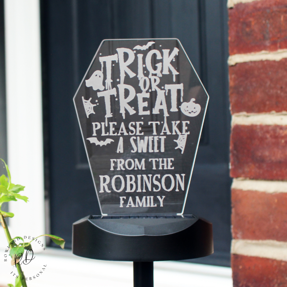 Halloween-themed sign with personalised text on a black stand against a door and brick wall background.