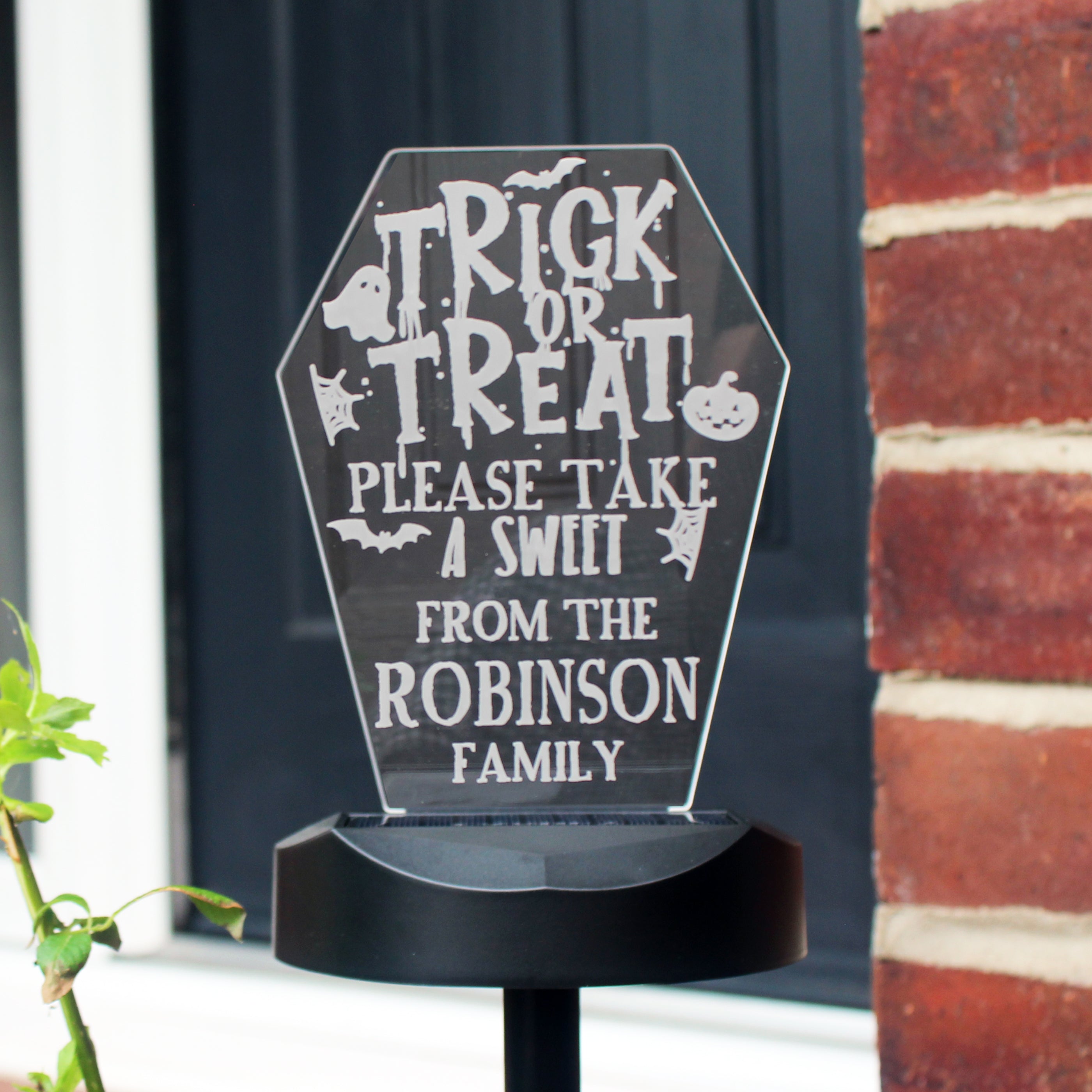 Halloween-themed sign with text 'Trick or Treat, please take a sweet from the Robinson family' on a black background.