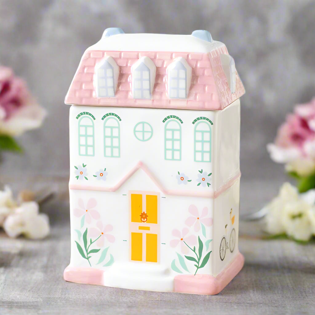  A charming pastel pink house-shaped ceramic oil burner and wax warmer, designed for home decor and relaxation. Features a removable roof, perfect for fragrance oils or wax melts, with a tealight candle holder beneath.