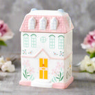  A charming pastel pink house-shaped ceramic oil burner and wax warmer, designed for home decor and relaxation. Features a removable roof, perfect for fragrance oils or wax melts, with a tealight candle holder beneath.