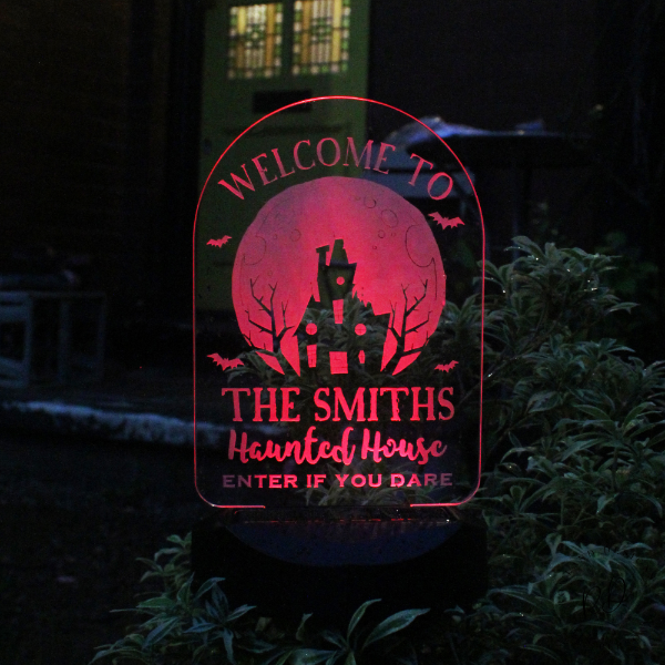 Decorative sign with 'Welcome to The (your family name) Haunted House' text in a dark setting