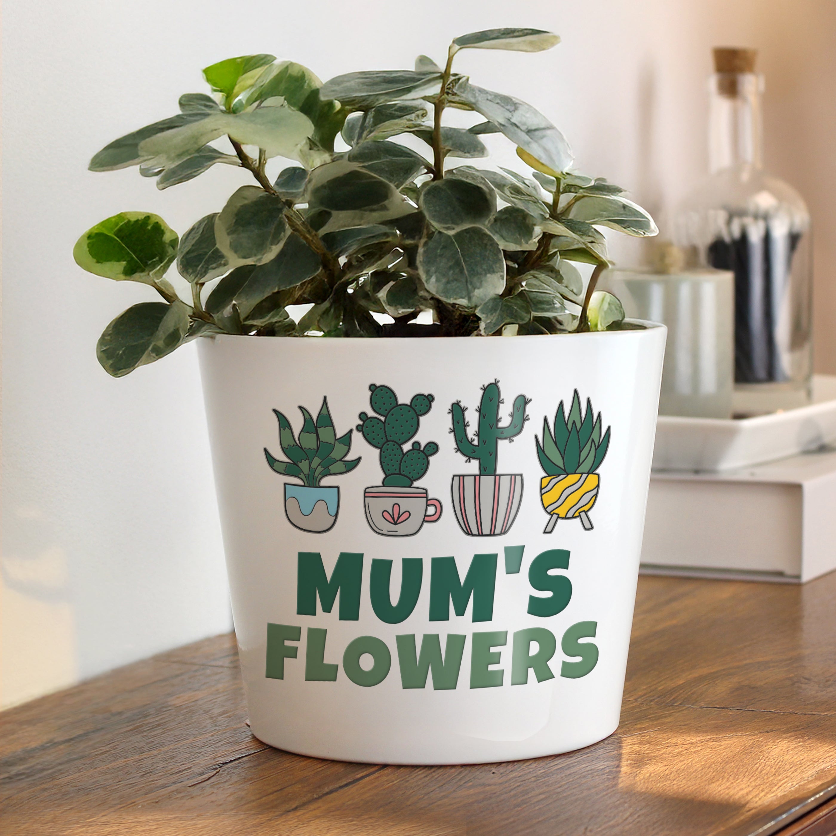 Potted plant in a white pot with 'Mum's Flowers' text on a wooden surface.