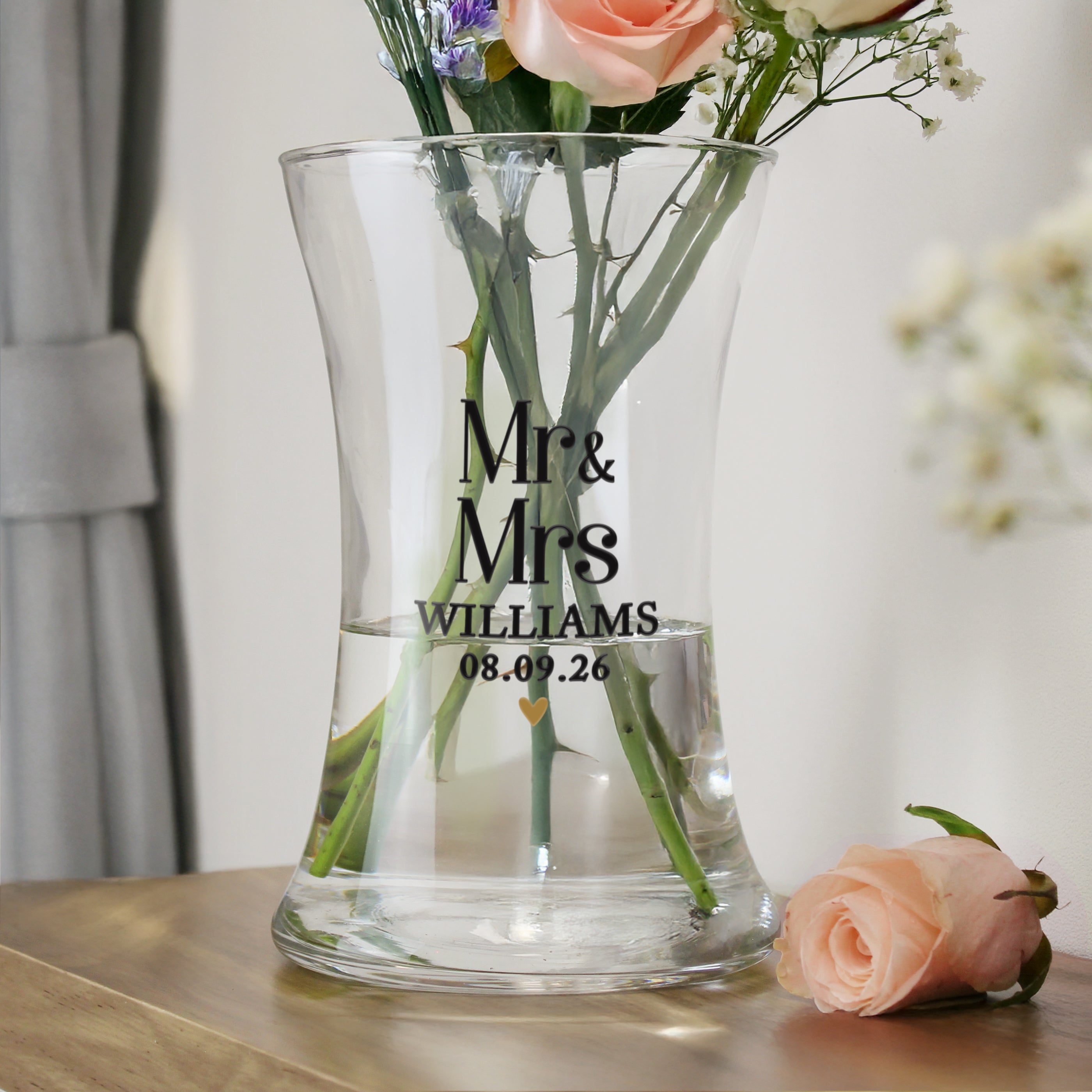 Clear glass vase with engraved 'Mr & Mrs Williams' and flowers on a wooden surface.