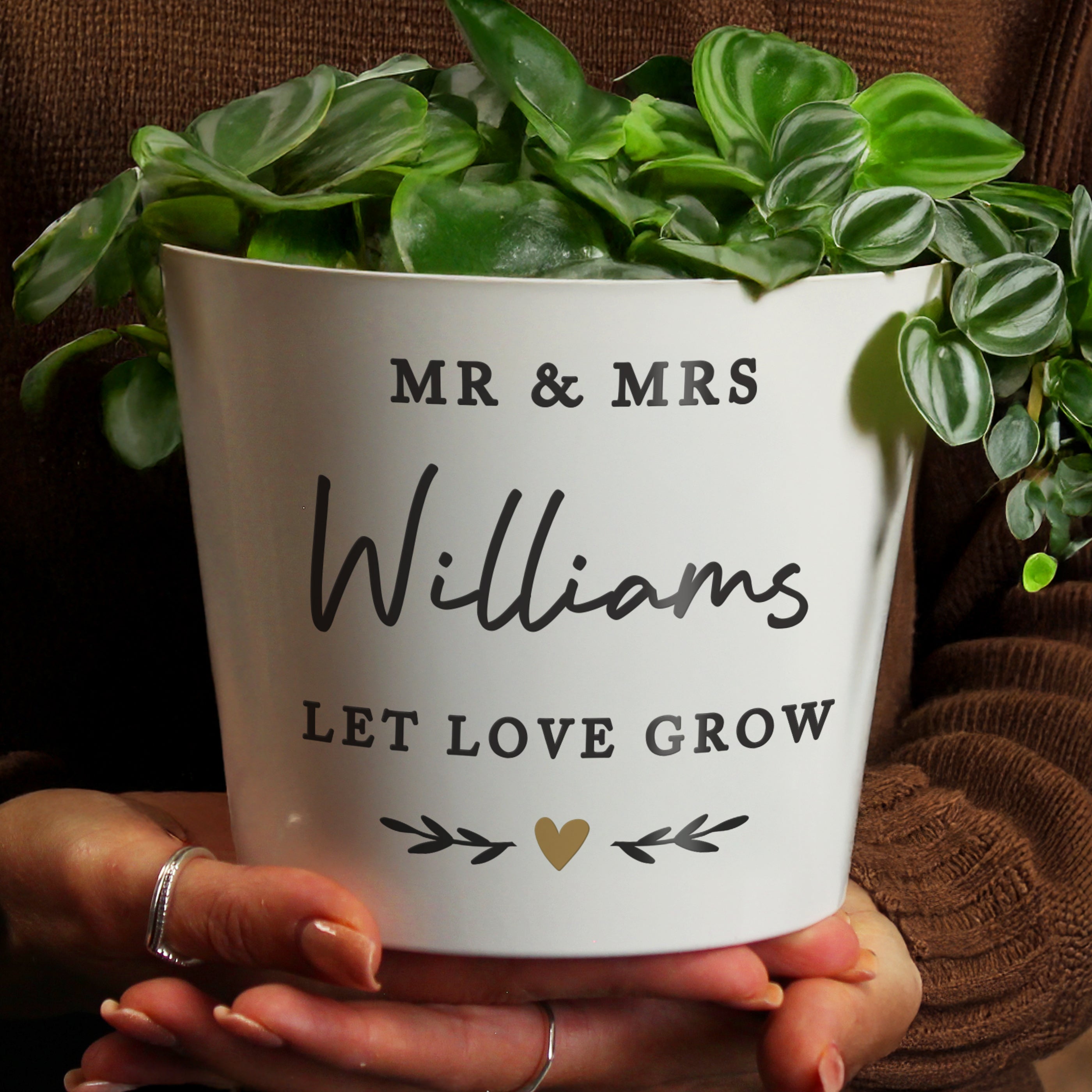 White pot with green plant labeled 'MR & MRS Williams LET LOVE GROW' held by hands.