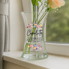 Clear glass vase with floral design and text on a windowsill
