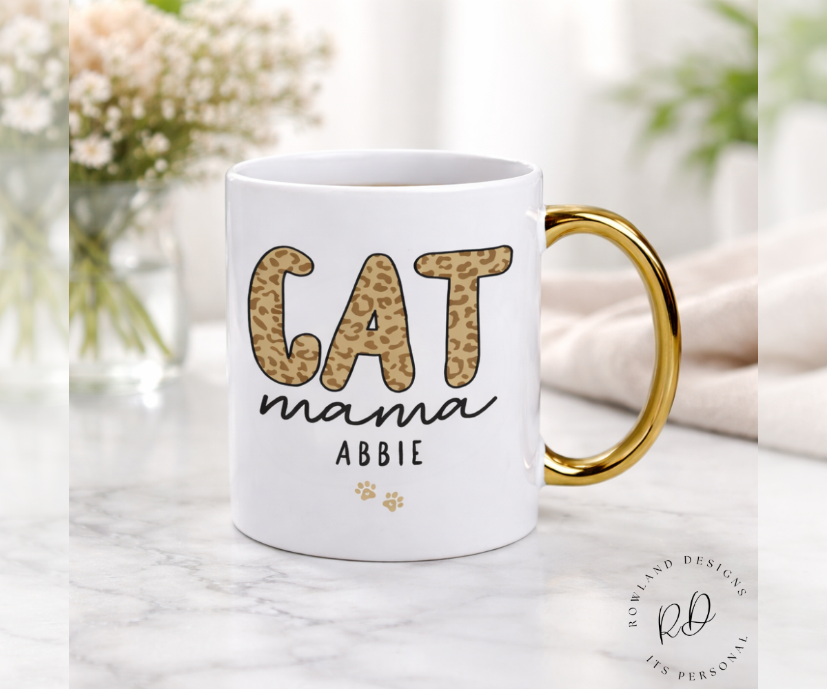 White mug with gold handle featuring 'CAT mama ABBIE' text on a marble surface.