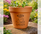 Terracotta pot with 'Lily's Flower Garden' text on a wooden surface with a garden background.