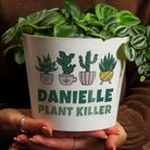 White pot with cactus designs and 'Danielle Plant Killer' text, held by a person.