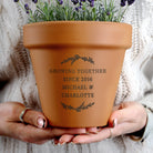 Terracotta pot with engraved message held by hands against a textured fabric background