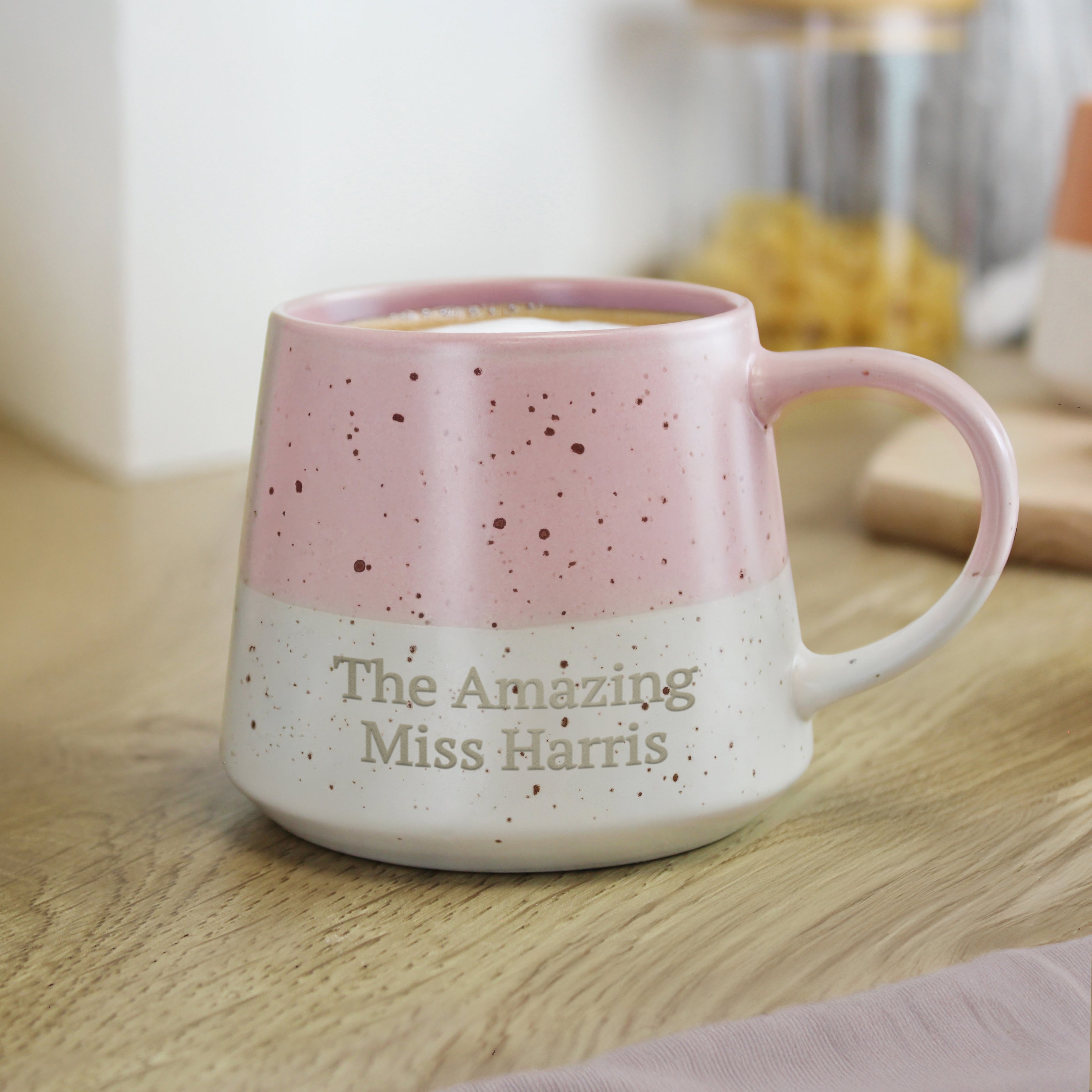 Pink speckled mug with 'The Amazing Miss Harris' text on a wooden surface.