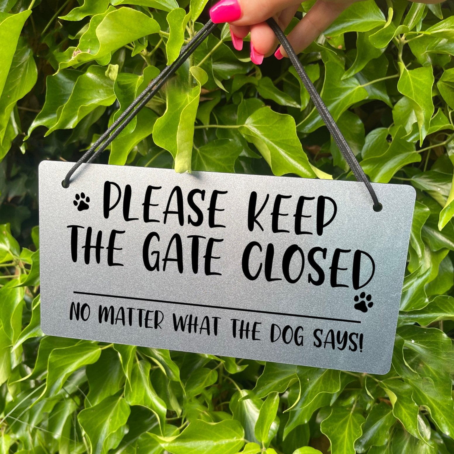 "Silver Laser-Engraved 'Please Keep the Gate Closed' Sign with Paw Print Illustration" Description: Close-up of a silver-colored acrylic sign with laser-engraved text that reads "Please Keep the Gate Closed, No Matter What the Dog Says." The sign features a cute paw print illustration, adding a playful touch.