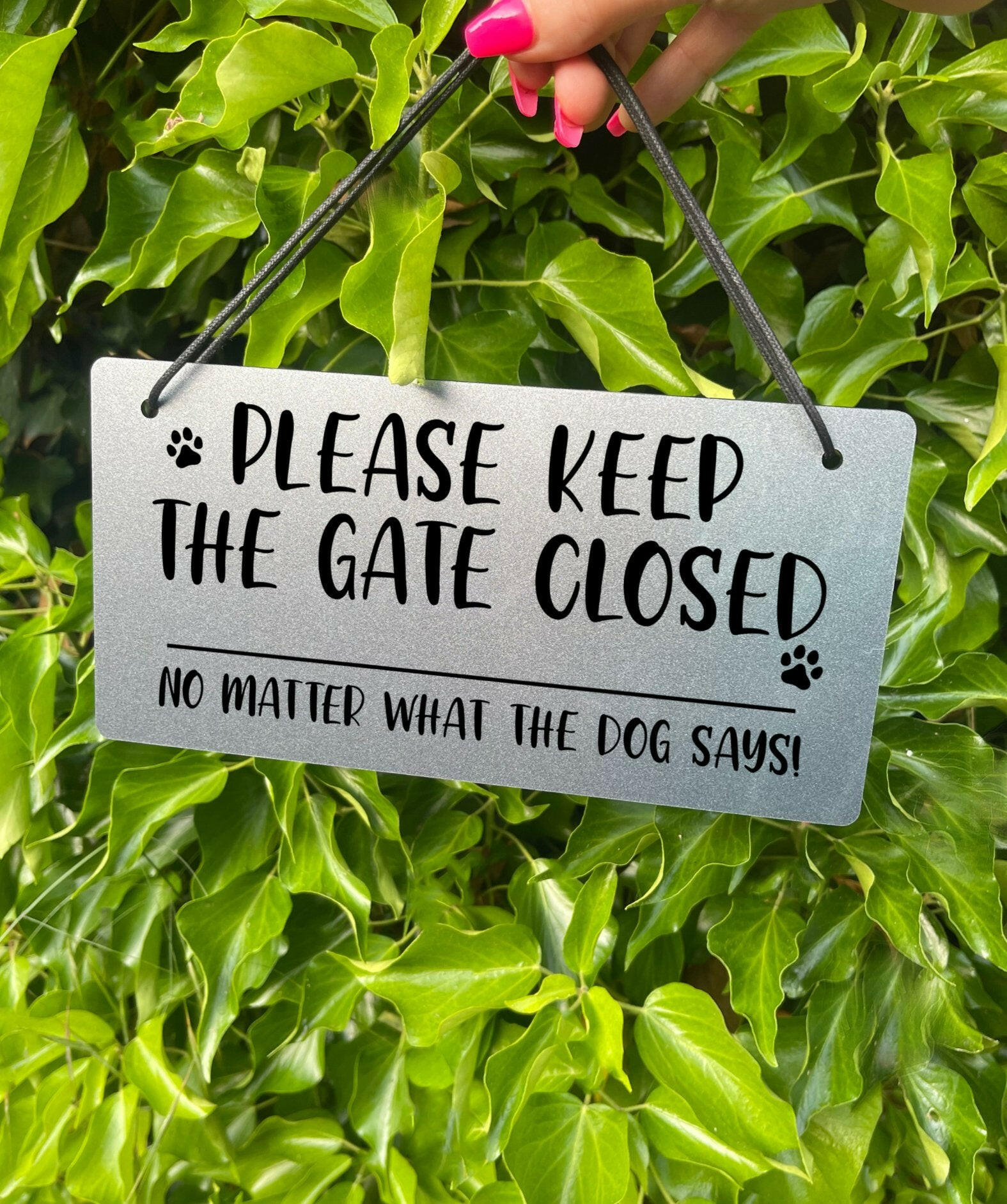 "Silver Laser-Engraved 'Please Keep the Gate Closed' Sign with Paw Print Illustration" Description: Close-up of a silver-colored acrylic sign with laser-engraved text that reads "Please Keep the Gate Closed, No Matter What the Dog Says." The sign features a cute paw print illustration, adding a playful touch.