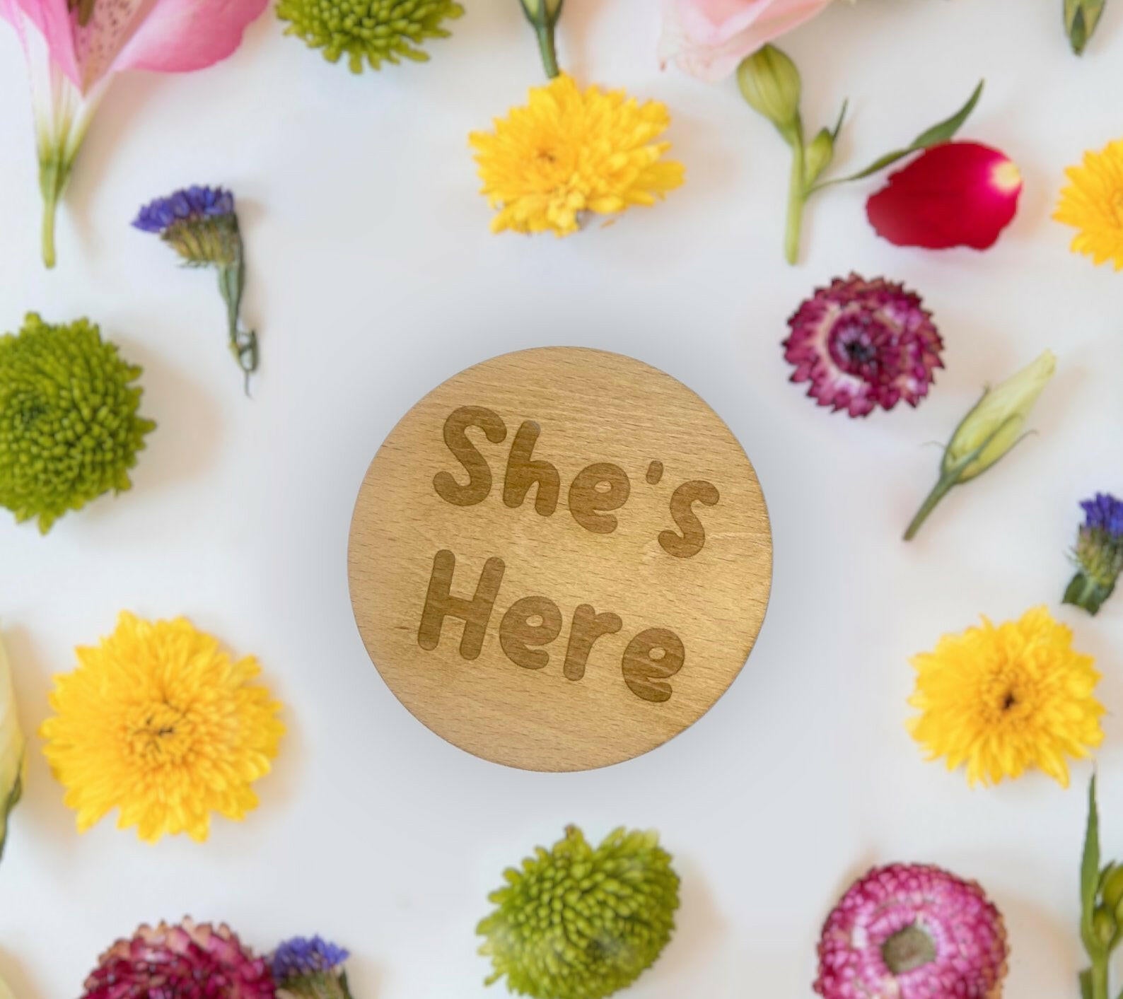 A "He's Here, She's Here" plaque next to a hospital wristband, creating a sentimental memory.