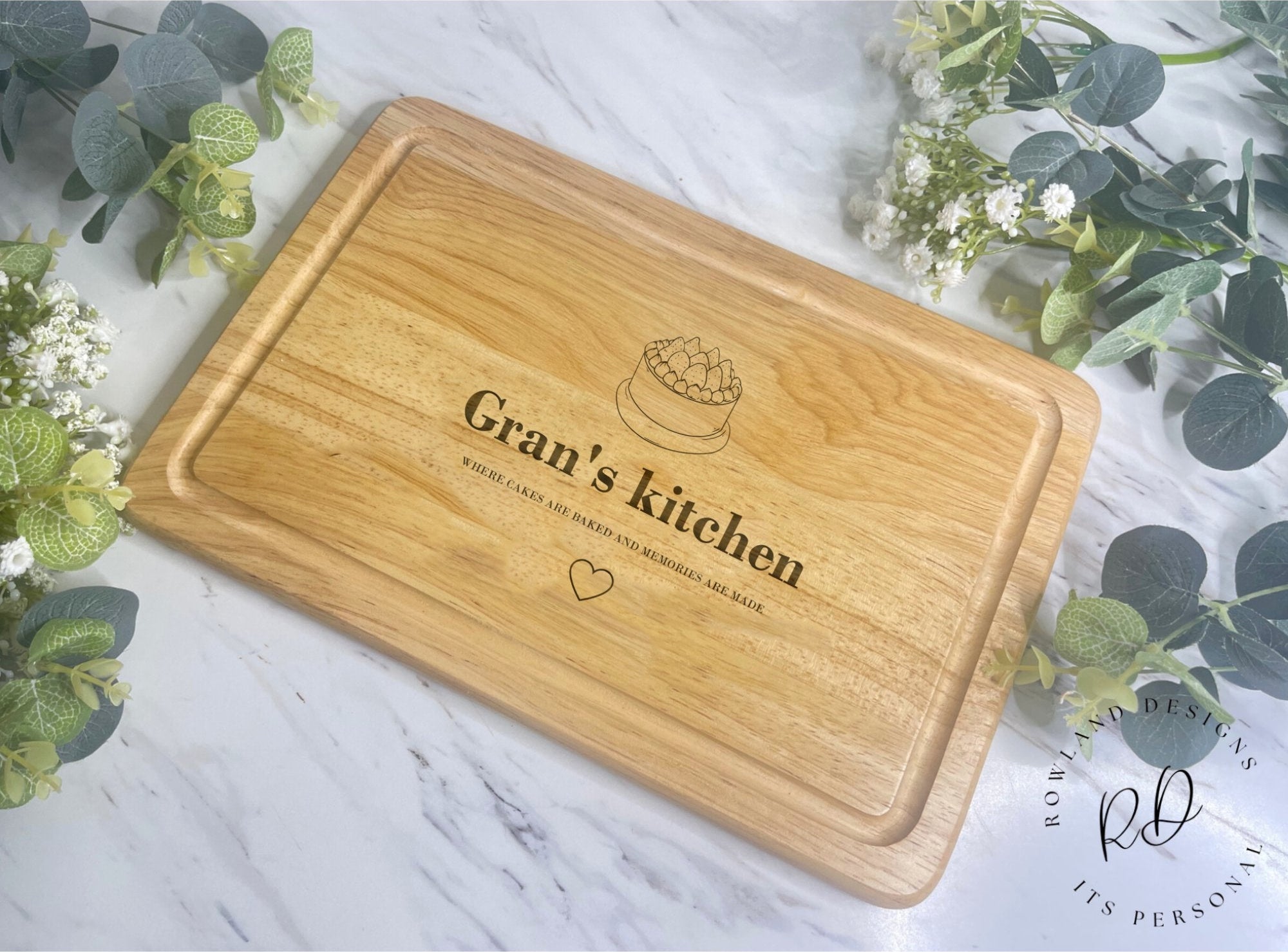 A personalised wooden chopping board with a cake and heart icon and custom engraved text.