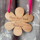 Flower-shaped wooden baby pram sign engraved with “Please don’t touch” message, with pink ribbon.

