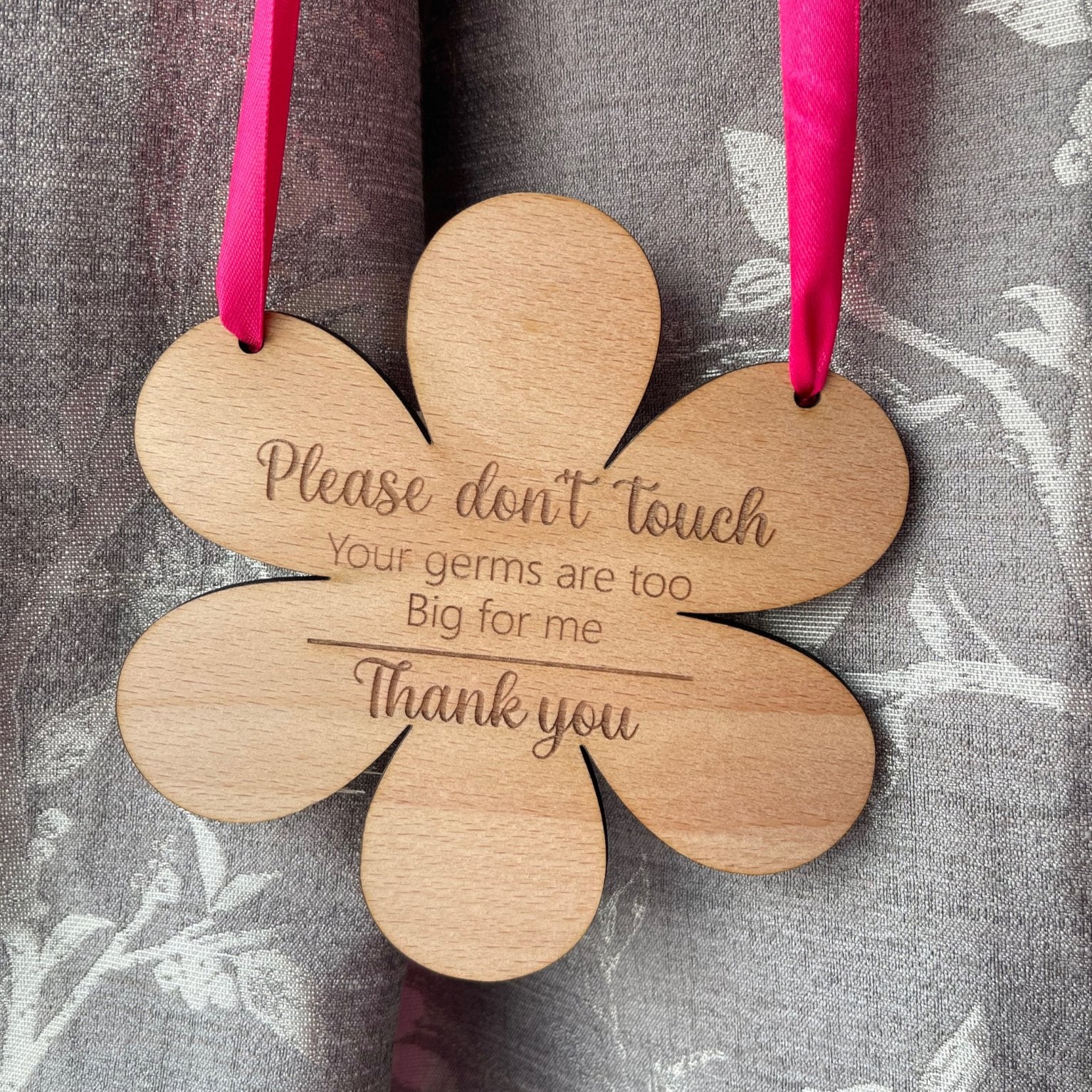 Flower-shaped wooden baby pram sign engraved with “Please don’t touch” message, with pink ribbon.

